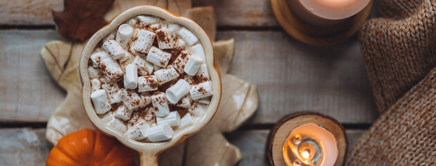 Flat lay top view. Spicy sweet fall hot drink: delicious pumpkin latte with cinnamon, marshmallow. Served in handmade artisan mug in shape of pumpkins, cozy home decor with candles, dry leaves banner