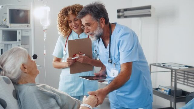 Elderly doctor and a medical nurse talk to an old grandmother patient lying in the ward, tell her good news and give support by touching her hand