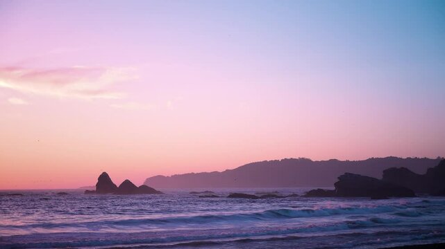 atardecer en una playa con cielo de colores rojo y violeta olas suaves rocas grandes y aves volando