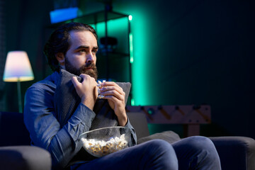 Sad man watching drama movie on online streaming service in apartment, enjoying time off from work. Person on couch hugging pillow, feeling affected by film broadcasted on TV