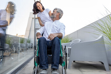 Dark-haired woman carrying a wheelchair of her husband