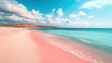 Wide view of a pink sand beach with turquoise ocean and red cliffs in the distance under a partly cloudy sky