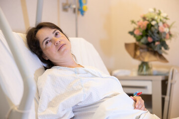 Tired calm adult woman, connected to IV, resting in bed in cozy modern hospital room after...