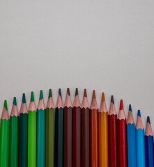 A row of colored pencils are lined up on a white background. The pencils are of various colors, including green, brown, red, and blue. Concept of creativity and artistic expression