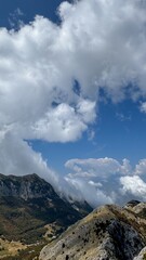 A dramatic scene of rugged mountain peaks partially covered by dense clouds, with clear blue sky peeking through. 