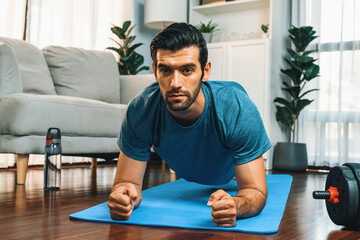 Athletic and sporty man doing plank on fitness mat during home body workout exercise session for fit physique and healthy sport lifestyle at home. Gaiety home exercise workout training.