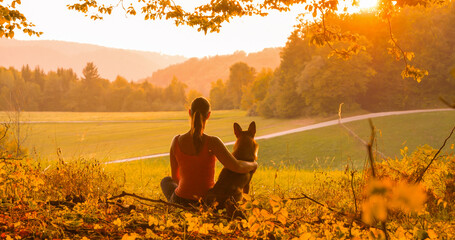 SILHOUETTE, LENS FLARE: Young lady and her dog share a peaceful moment watching sunset. Genuine...