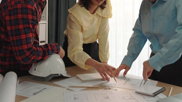 Smart architect and safety engineer discussion about building blueprint on table with architectural document, measurement tools and wooden block scatter around at modern office. Closeup. Delineation.