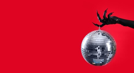 Black hand of witch with disco ball on red background with space for text. Halloween celebration