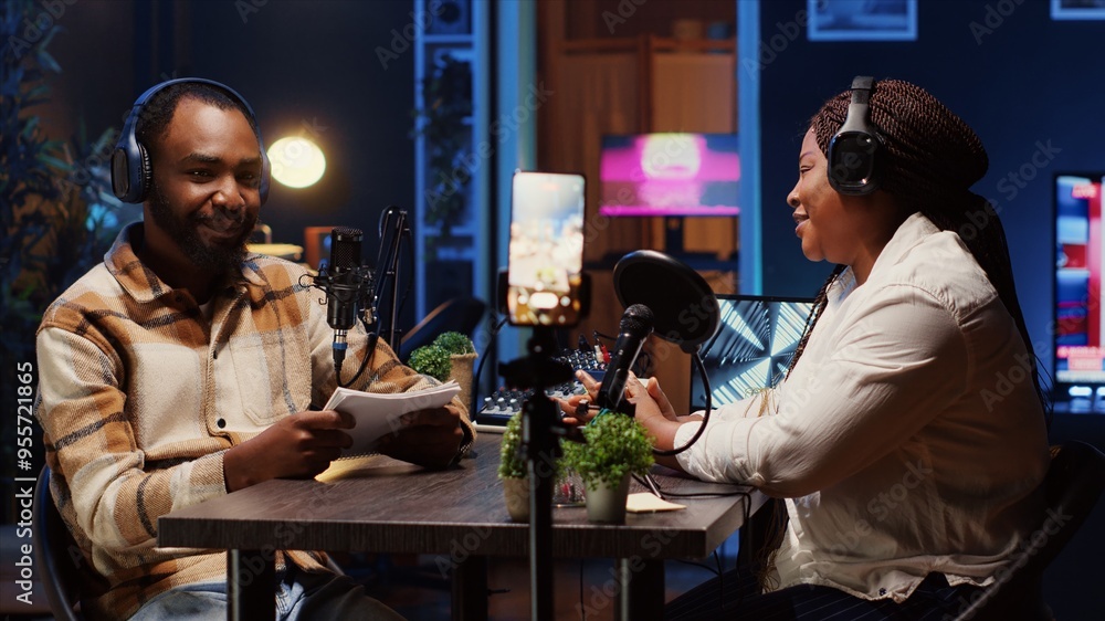 Poster podcast host using smartphone on tripod to record guest telling interesting story to fans watching d