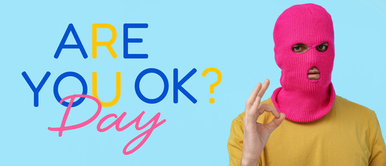 Handsome young man in balaclava showing OK gesture on blue background © Pixel-Shot