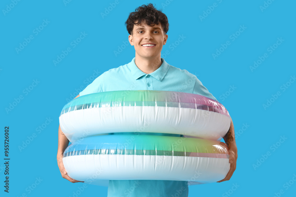 Wall mural young man with inflatable rings on blue background