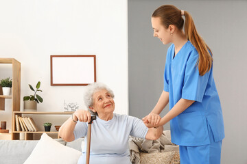 Female caregiver helping senior woman to stand up at home