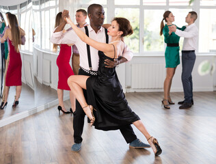 Woman paired with African American man practices movements of Latin tango dance and trains to...