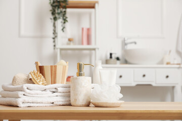 Soap dispenser, shower sponge, folded towels and bath accessories on wooden table in bathroom,...