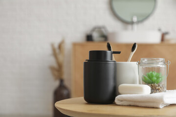 Bar of soap, dispenser, towel, houseplant and cup with toothbrushes on table in bathroom, closeup