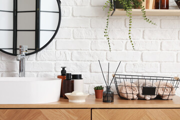 Sink bowl and bath accessories on wooden cabinet near white brick wall