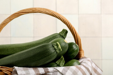 Wicker basket with fresh zucchini near white tile wall