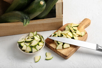 Wooden box with many fresh zucchini and bowl of slices on white background