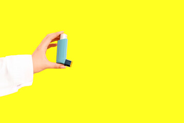 Female doctor hand with inhaler on yellow background