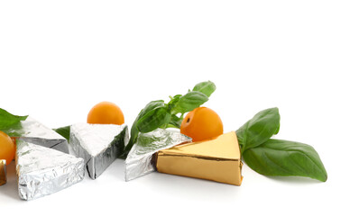 Triangles of tasty processed cheese in foil, cherry tomatoes and basil leaves on white background, closeup