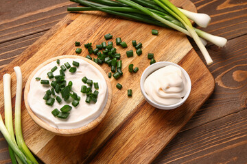 Bowls of tasty sour cream with sliced green onion on wooden background