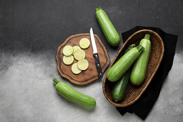 Board of slices and wicker bowl with fresh green zucchini on grey background