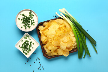 Bowls of tasty sour cream with sliced green onion and potato chips on blue background