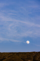 The almost  full crescent moon rises over the Iguaque mountain, in the eastern Andes of central Colombia, on a fairy clear sky at the beginning of the sunset.