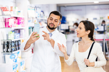 Male pharmacist consulting woman buyer about drug in drugstore.