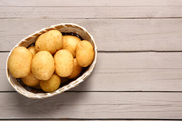 Wicker bowl with raw baby potatoes on grey wooden background