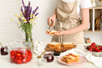 Woman preparing tasty toasts with sweet strawberry jam at table in kitchen