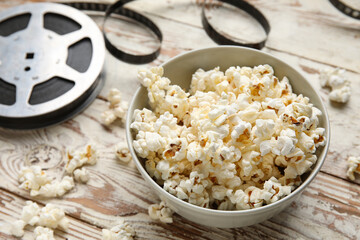 Bowl with tasty popcorn and film reel on white wooden background