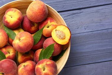 Bowl with sweet peaches and leaves on blue wooden background