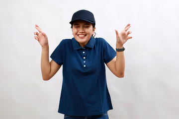 Young asian woman courier wearing delivery uniform and cap gesturing finger crossed smiling with hope and eyes closed. luck and superstitious concept.