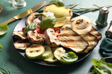 Plate with tasty grilled vegetables on green background
