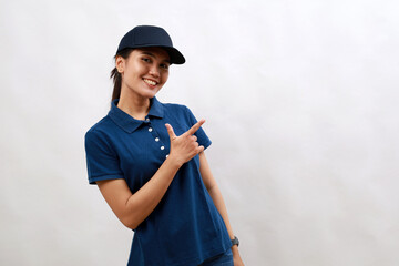 Young asian woman courier wearing delivery uniform and cap cheerful with a smile of face pointing with hand and finger up to the side with happy and natural expression on face