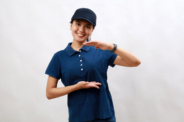Young asian woman courier wearing delivery uniform and cap gesturing with hands showing big and large size sign, measure symbol. smiling looking at the camera. measuring concept.
