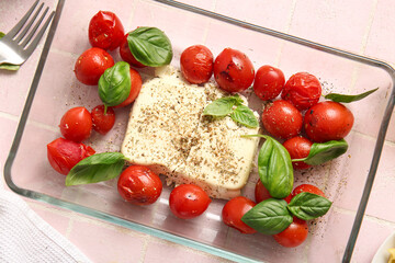 Baking dish with tasty tomatoes and feta cheese on pink tile background