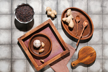 Wooden tray with ginger, garlic, rice and cutting board on grey tile background