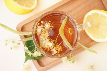 Board with glass cup of linden tea and lemon on beige background