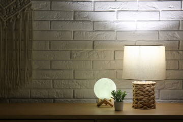 Different glowing lamps and houseplant on wooden table in dark room