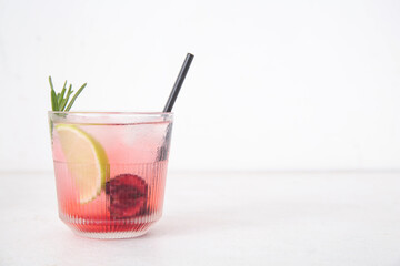 Glass of tasty cherry lemonade with lime and rosemary on white background