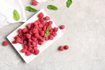 Plate with fresh raspberries and mint on grey background