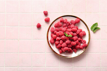 Plate with fresh raspberries and mint on pink tile background