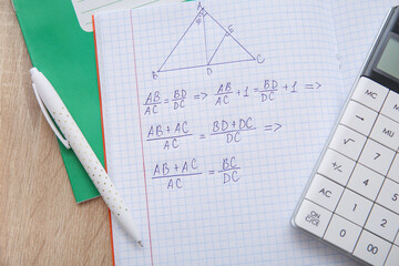 Open copybook with formulas, calculator and pen on wooden table