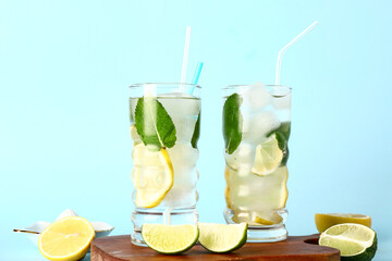 Wooden board with glasses of cold mojito and citrus fruits on color background