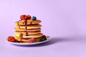 Plate of tasty pancakes with raspberries and blueberries on lilac background