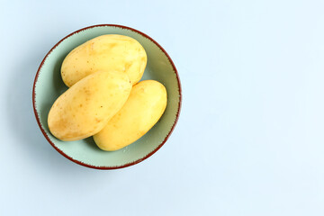 Bowl with raw potatoes on blue background