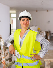 Portrait of a young attractive woman engineer in uniform standing near a stepladder in an apartment...